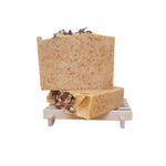 Two soap bars with visible paprika topped with roses on a wooden soap dish against a white background