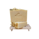 Two bars of soap with calendula on top on a wooden stand with a white background