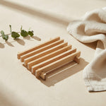 Rectangular slatted wooden soap dish on a warm neutral spa surface