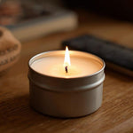 Candle in a tin container on a wooden surface with a blurred background