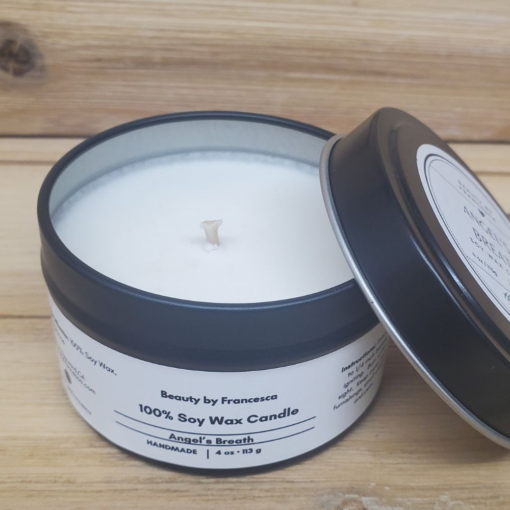 Angel's Breath Candle in a black tin with lid resting against it against a wood background