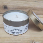 Angel's Breath Candle in a gold tin with lid resting against it against a wood background