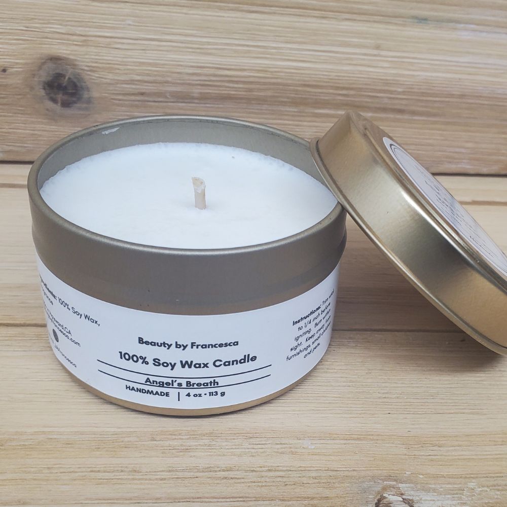 Angel's Breath Candle in a gold tin with lid resting against it against a wood background