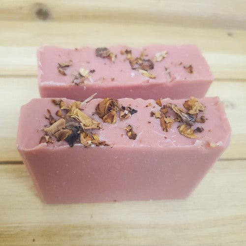 Two pink soap bars with dried roses on a wooden surface