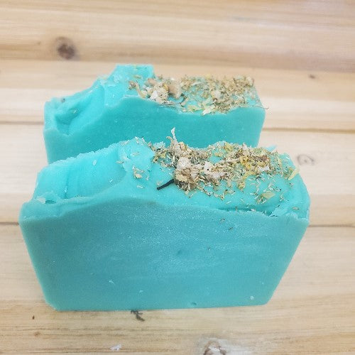 Two green  soap bars decorated with chamomile on top on a wooden surface
