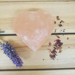 Heart Shaped Pink Himalayan salt Body Massage Stone on a wooden surface with lavender and dried roses