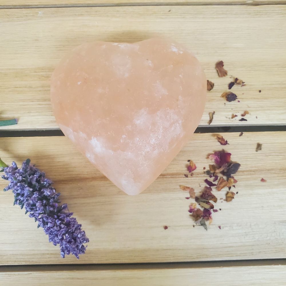 Heart Shaped Pink Himalayan salt Body Massage Stone on a wooden surface with lavender and dried roses