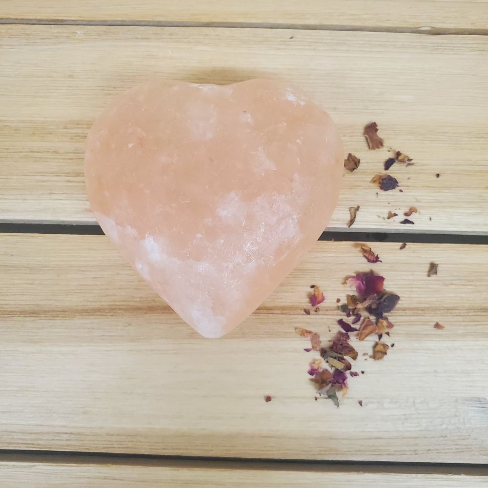 Heart Shaped Pink Himalayan salt Body Massage Stone on a wooden surface with dried roses