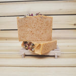Two bars of paprika soap with floral elements on a wooden stand against a wooden background