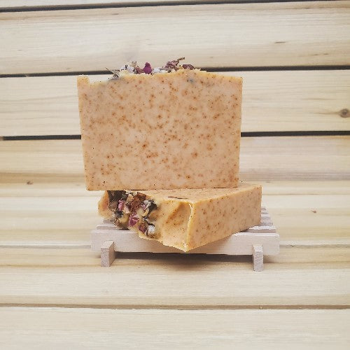 Two bars of paprika soap with floral elements on a wooden stand against a wooden background