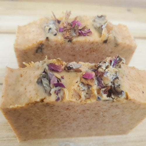 Two bars of paprika soap topped with dried roses on a wooden surface