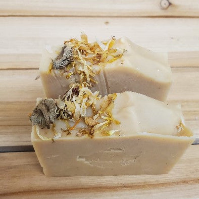 Two bars of soap with calendula on top on a wooden surface