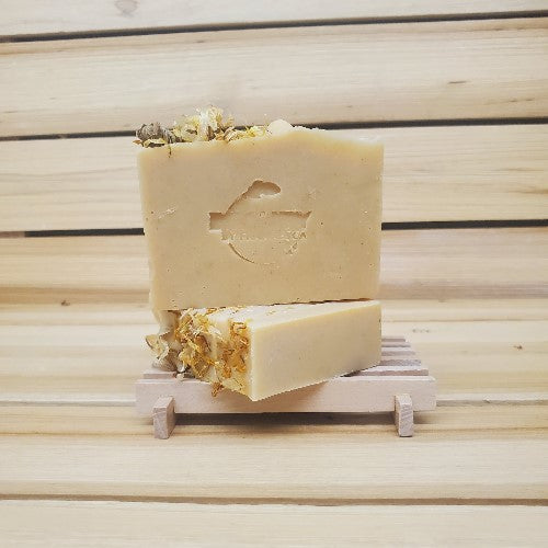 Two bars of soap with floral elements on a wooden stand against a wooden background