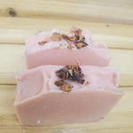 Two pink soap bars topped with roses on a wooden surface