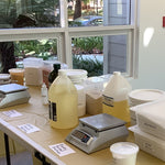 Table with various ingredients and a scale in a room with large windows showing outdoor scenery.