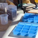 Blue silicone soap mold trays on a table with containers of lavender and chamomile in the background.