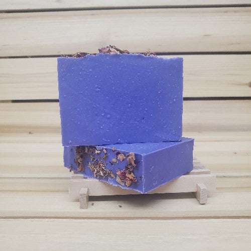 Two purple reign soap bars with dried roses on a wooden stand against a wooden background