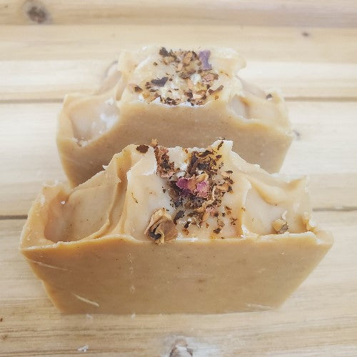 Top View of Two bars of turmeric infused soap topped with roses against a wood background