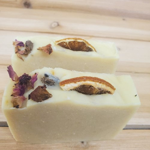 Two soap bars decorated on top with an orange slice and roses on a wooden surface