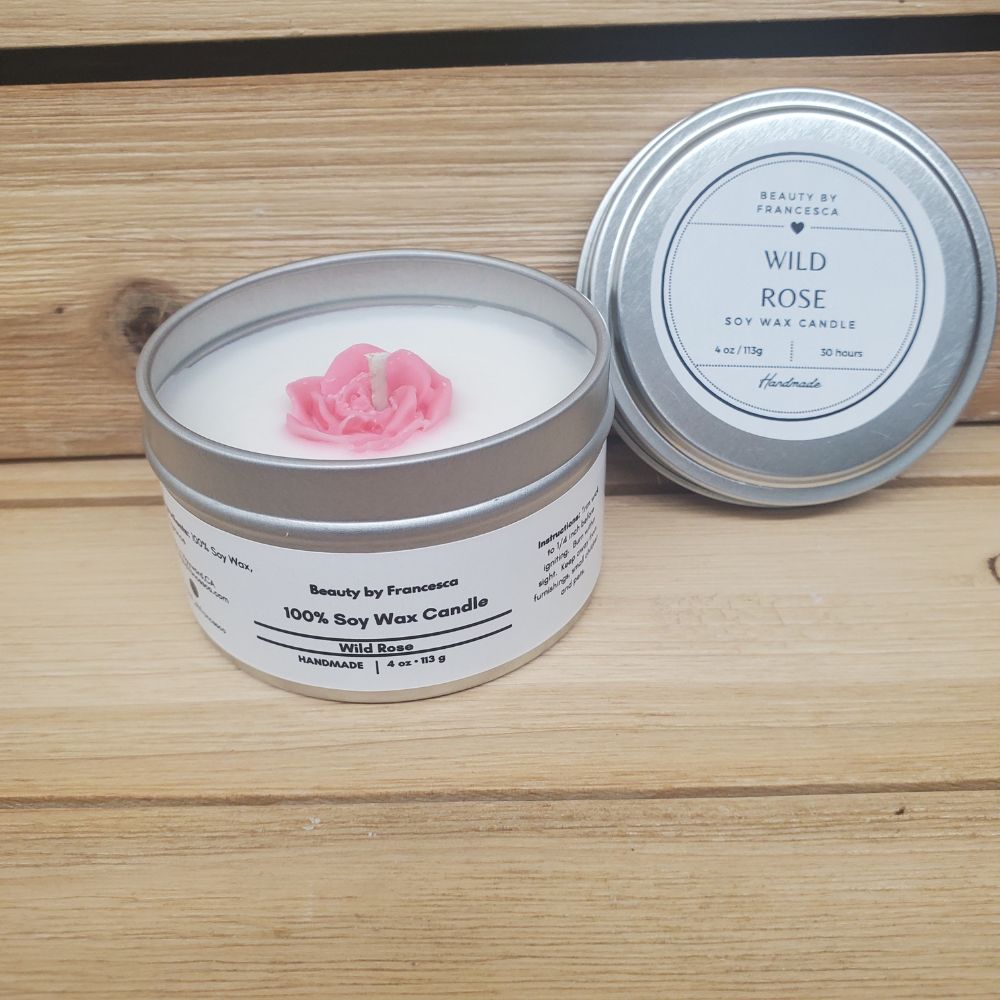 Wild Rose Soy Candle in a tin with a pink rose on a wooden surface