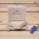 2 bars of lavender orange soap on a soap dish next to a sprig of lavender against a wood background