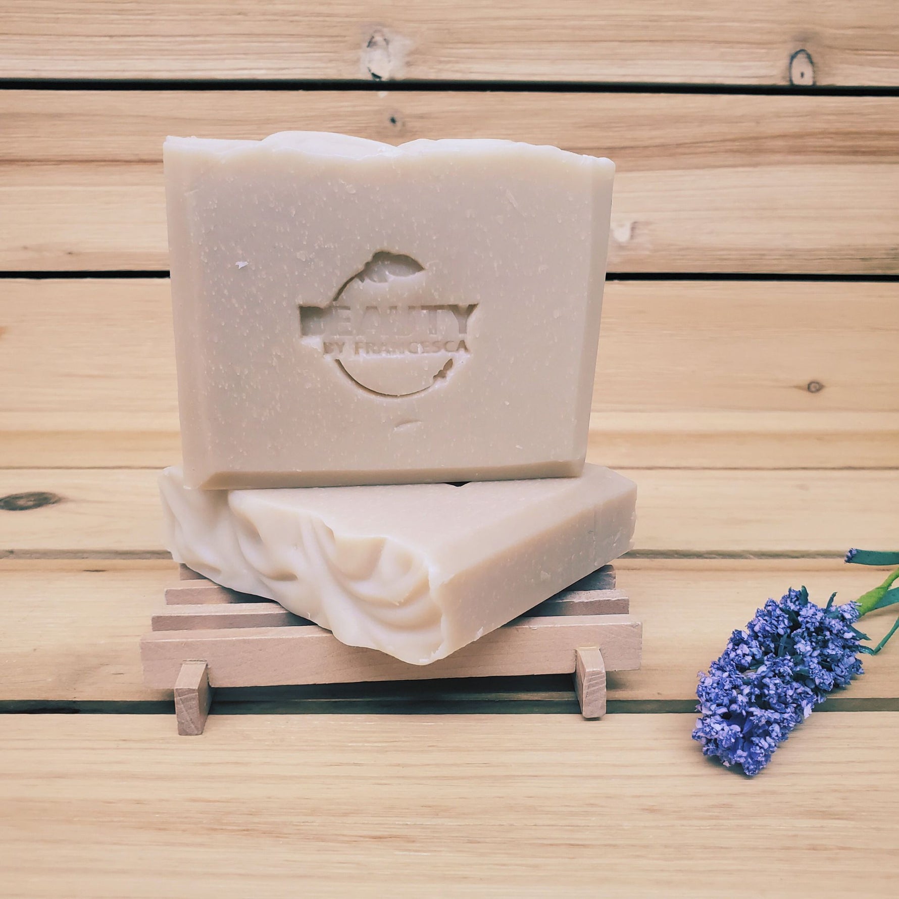 2 bars of lavender orange soap on a soap dish next to a sprig of lavender against a wood background