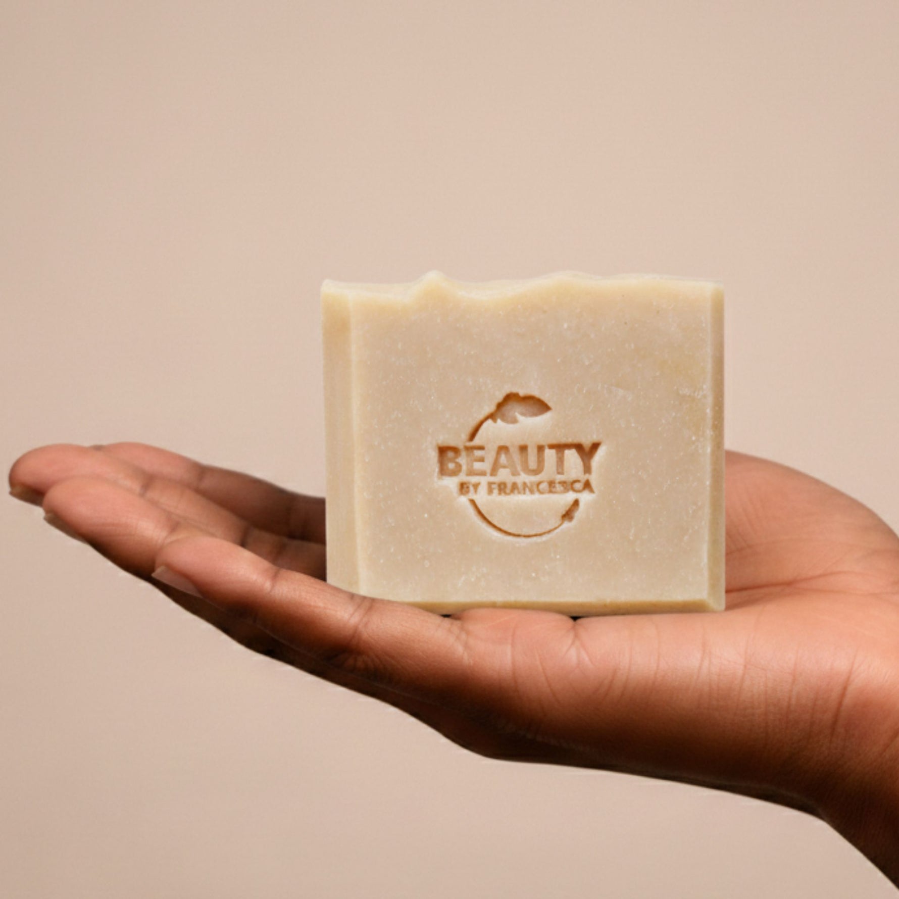 Bar of lavender orange soap with 'Beauty by Francesca' branding held in a hand against a beige background