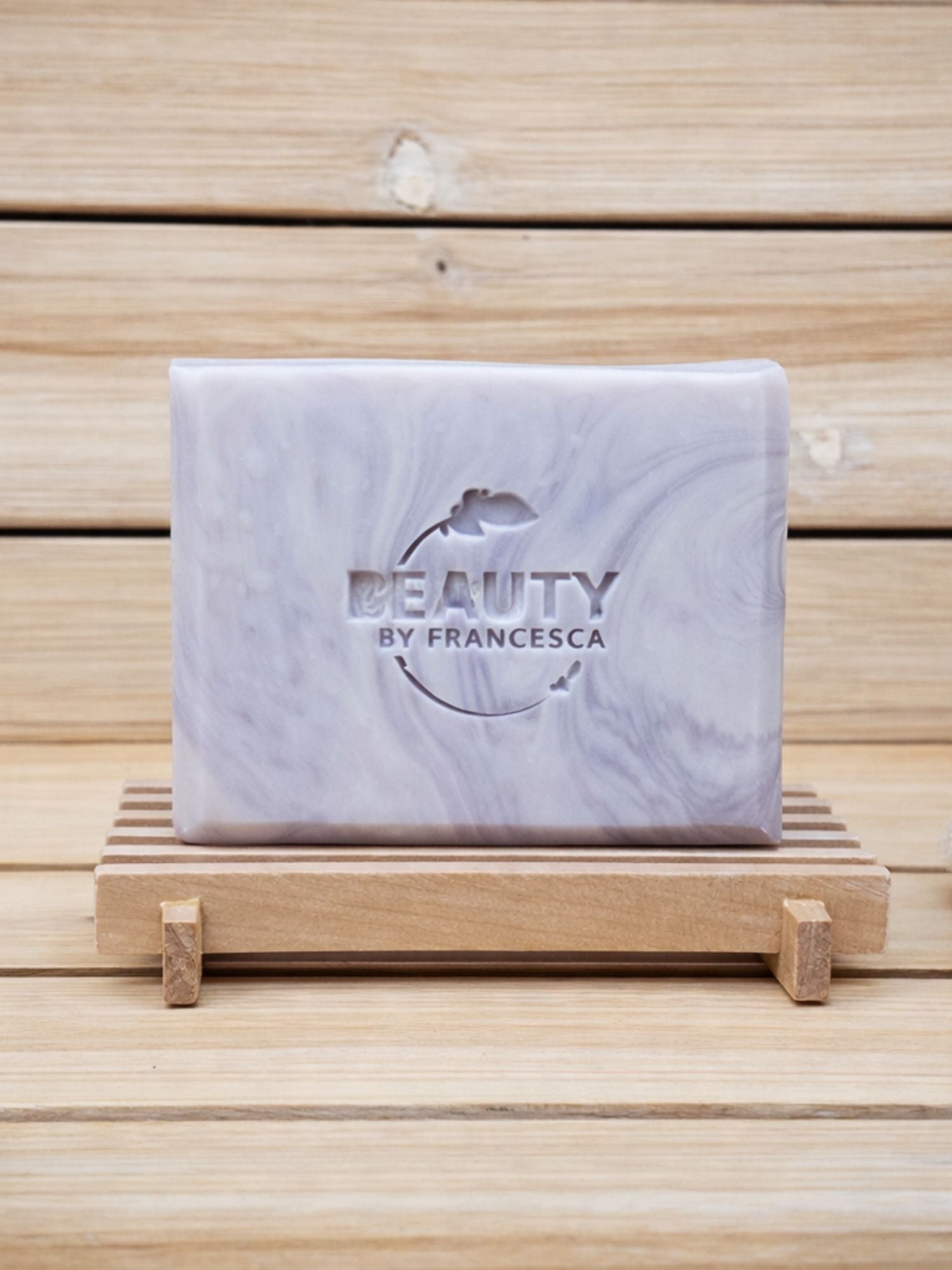 Marble-patterned lavender soap bar with 'Beauty by Francesca' branding on a wooden stand.