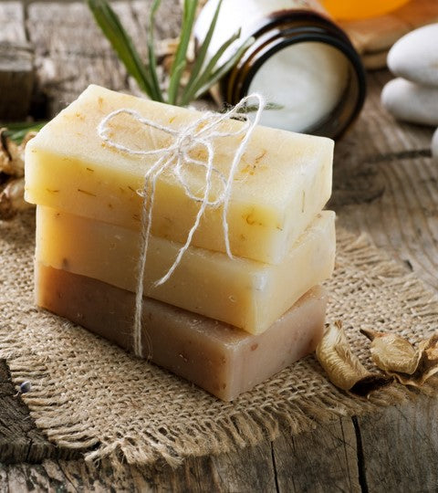 Three bars of soap stacked on a rustic wooden surface with a natural background.