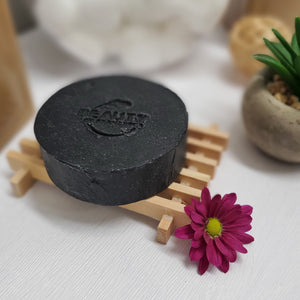 Activated Charcoal Soap on on wooden rack with flower and plant nearby