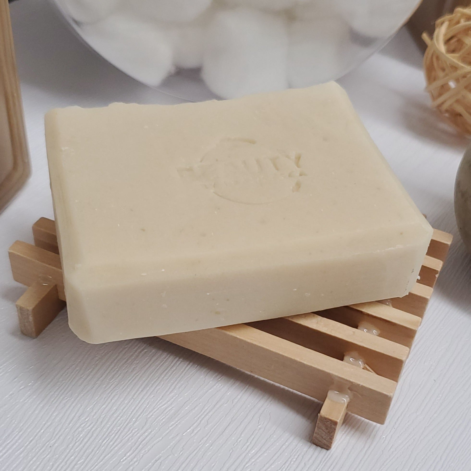 Coco shea coconut oil soap bar on wooden soap dish near cotton balls and plant